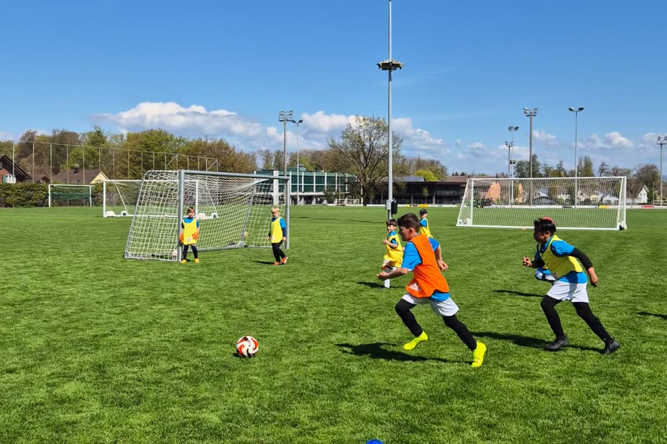 Kinder sprinten im Camp-Spiel zum Ball vor dem Tor