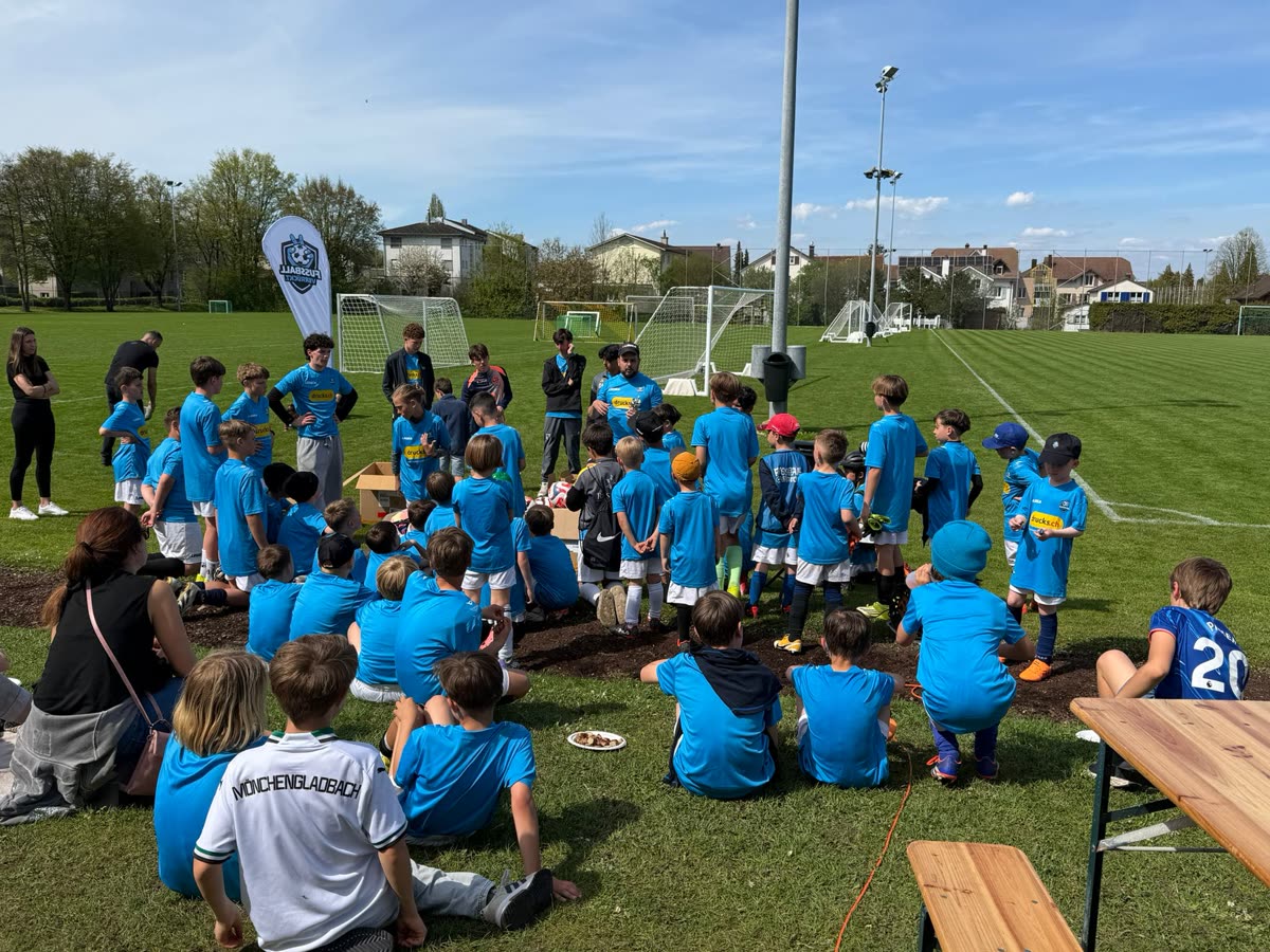 Kinder bilden im Camp einen grossen Kreis, daneben die fussballverrückt-Fahne