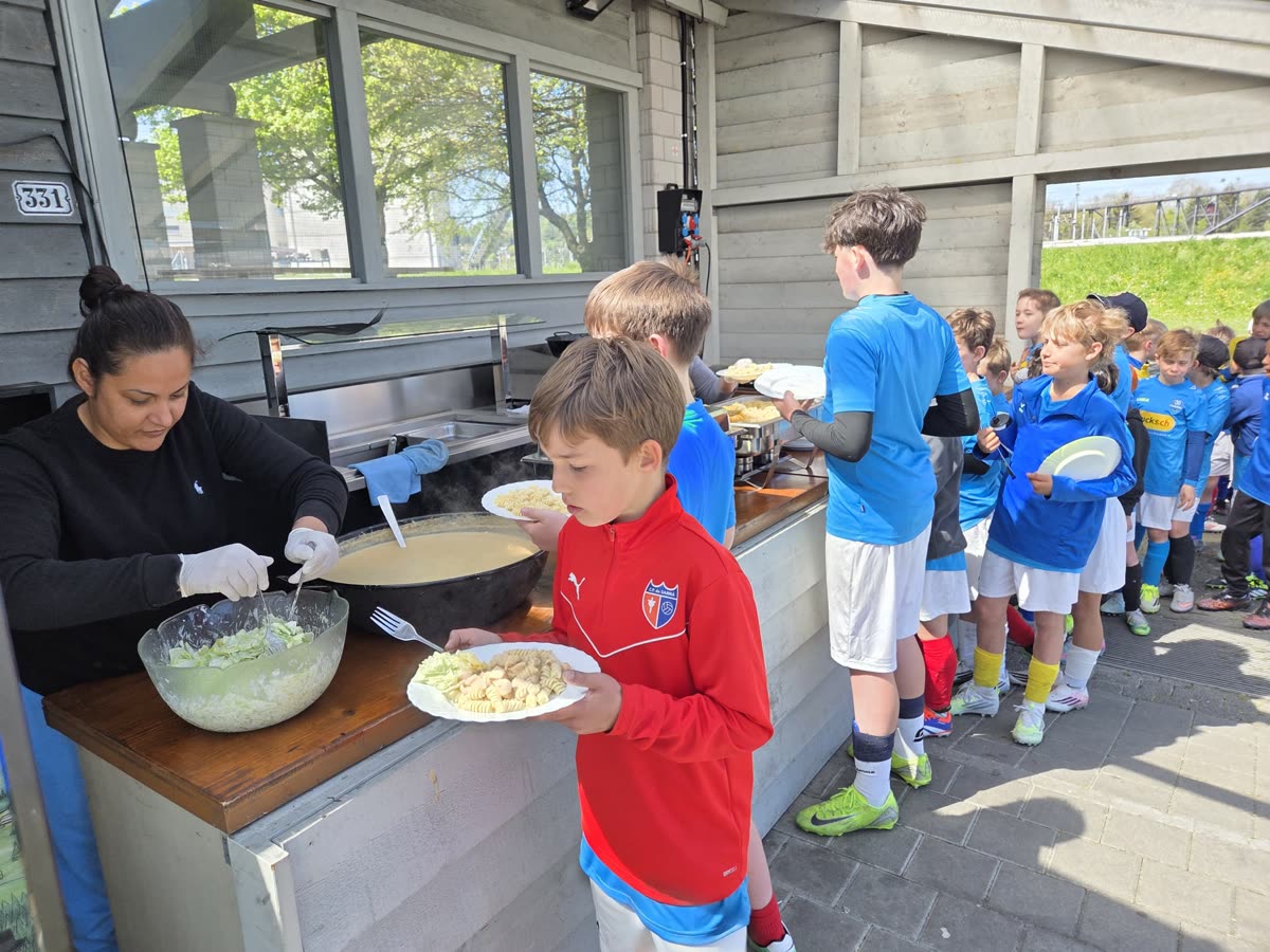 Mittagessen im Camp: Kinder stehen mit Tellern bei der Essensausgabe